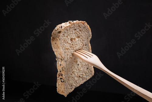 A piece of grain bread with wooden folk on balck background