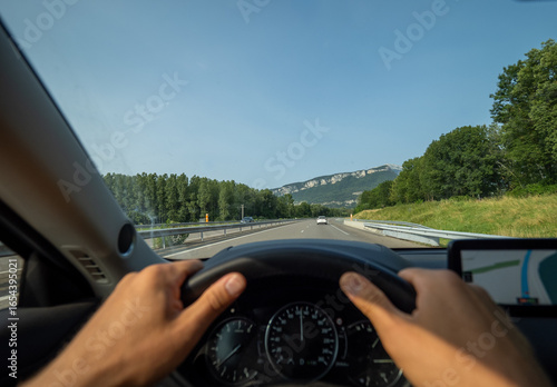 Gripping steering wheel while driving along winding mountain road, navigating GPS through scenic French Alpine landscape