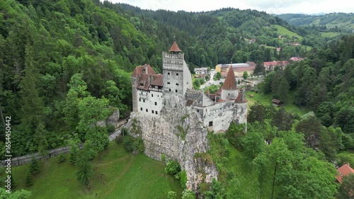 Wallpaper Mural Aerial view of imposing Bran Castle on a rocky hill, surrounded by lush green forests and a quaint village nestled in the valley, Bran, Județul Brașov, Romania. Torontodigital.ca