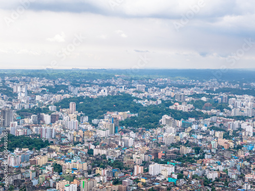 Wallpaper Mural Chattogram, Bangladesh - 15 August 2025: Aerial view of the bustling city, where buildings rise amidst green trees under a cloudy sky, showcasing a vibrant urban landscape. Torontodigital.ca