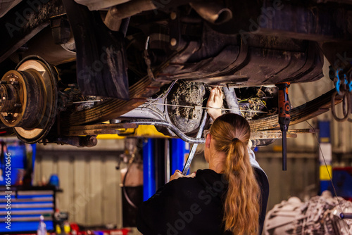 Female mechanic working on differential axel component underneath vehicle