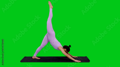 Young fit woman coach doing yoga downward facing dog split against green chroma key background