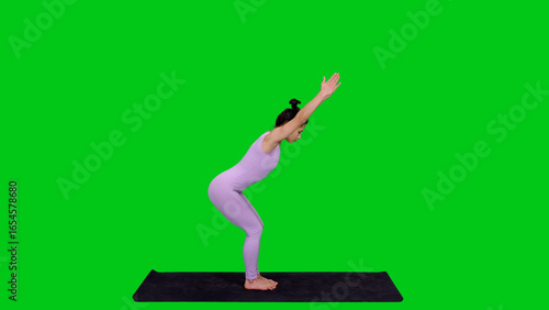 Young athletic woman in bodysuit practicing yoga chair posture on mat isolated on green background