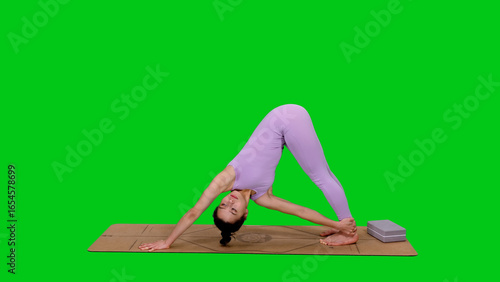 Young sporty woman in bodysuit doing triangle pose practicing yoga on green background	
