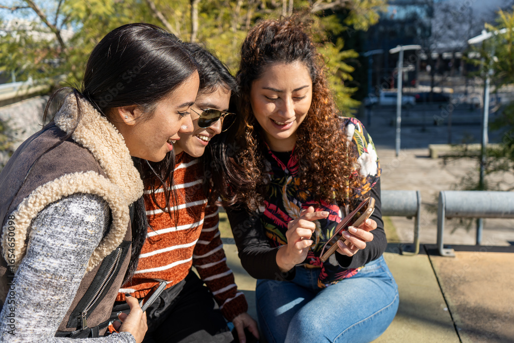 Naklejka premium Three young women sharing social media content on smartphone outdoors