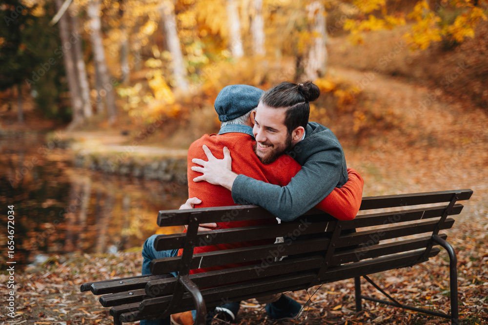 Fototapeta premium Grandad and grandson sitting on bench in park and hugging.