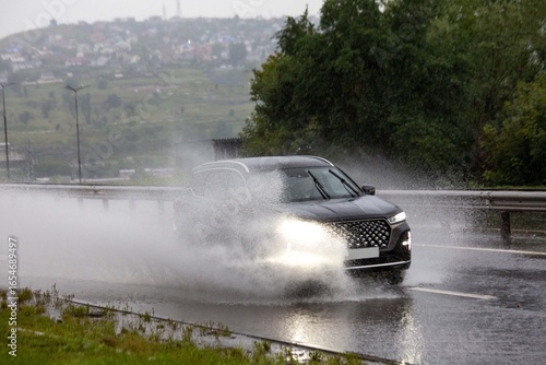 A car drives on a road flooded by rain. Heavy rainfall, climate change.