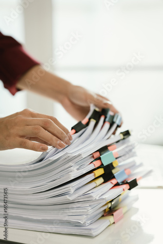 A woman in a red shirt is handling a large number of documents and files, symbolizing office work, documentation, organization, management, deadlines, workloads, bureaucracy, and business responsibili