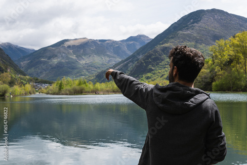 Billede på lærred Back view of unrecognizable male traveler sitting on pier near pond and enjoying
