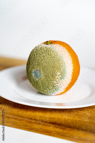 rotten orange fruit orange lies on a white plate on a wooden board, moldy orange fruit half bad