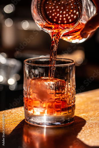 Billede på lærred Classic cocktail being poured through a strainer into a glass with a large ice c