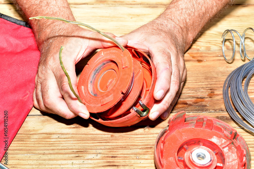 Repair of a petrol trimmer. Men's hands disassemble the head of a petrol trimmer.