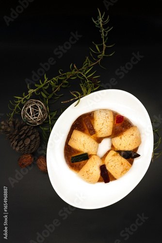 Mexican Three Kings bread with candied fruit, on black background, surrounded by pine cones, fresh rosemary, walnuts and metal sphere scribble