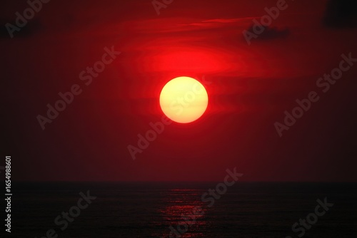 Dramatic sunset over ocean horizon with red sky and golden sun ball from low angle creating beautiful seascape