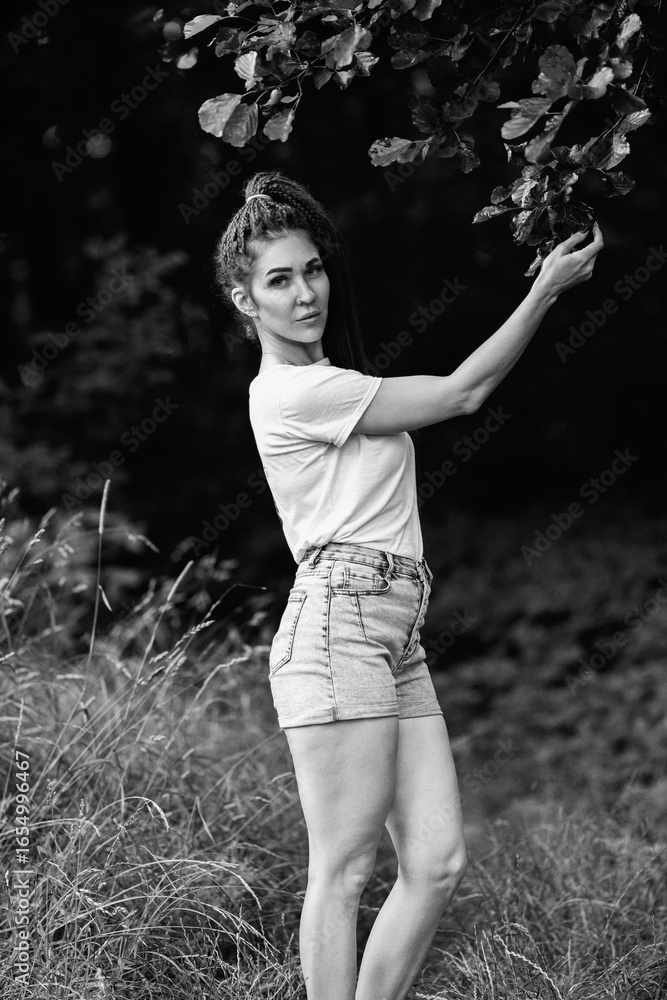 Portrait of a young beautiful girl in a T-shirt and shorts in a summer forest. Black and white photo. Portrait of a young beautiful girl in a T-shirt and shorts in a summer forest. Black and white photo.