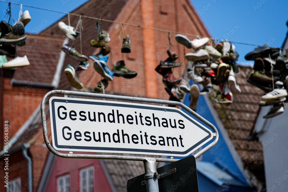 Obraz premium Street sign with arrow to Gesundheitshaus and shoes hanging on overhead wire in flensburg