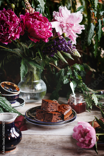 Delicious brownies on a plate. Pieces of a delicious chocolate cake on a plate with pion flowers. A chocolate cake served on a plate selective focus