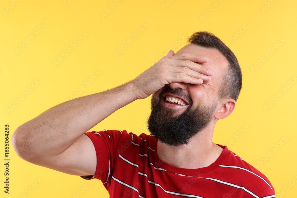 Fototapeta premium Man covering eyes and laughing on yellow background