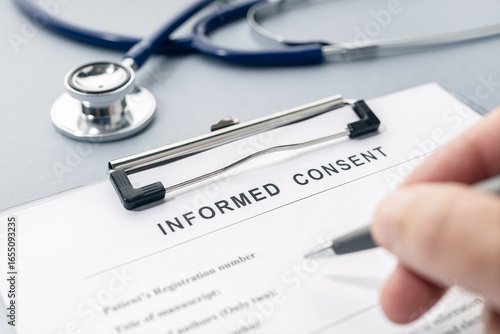 Hand filling a Informed Consent form and stethoscope on desk