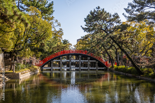 Red Sumiyoshi Taisha Sorihashi Bridge is a picturesque red bridge with a high arch that spans a tranquil pond in Osaka, Japan.