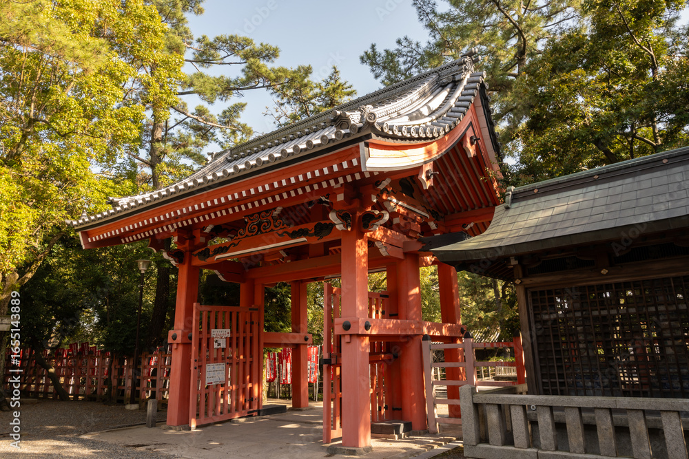 Naklejka premium A vibrant red torii gate with traditional Japanese architecture at Sumiyoshi Taisha in Osaka, Japan. Its an entrance to a Shinto shrine, showcasing intricate carvings and a rich history.