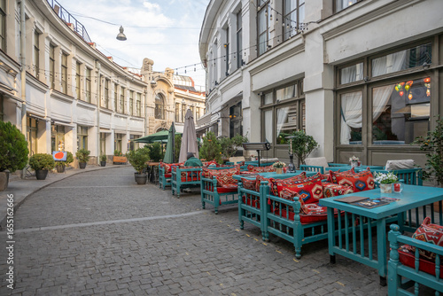 Obraz na plátně Outdoor cafe seating with teal tables and red cushions on old Tbilisi cobblestone street
