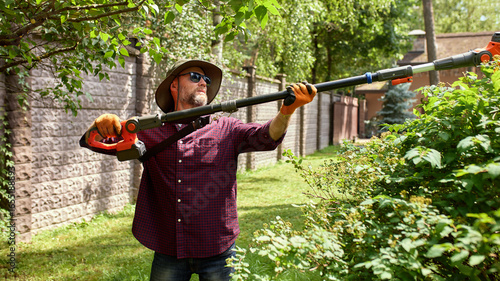 Fotografie Man trimming garden hedges with powered tool on a sunny day outdoors