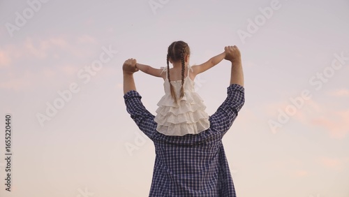 Photos concept father and daughter, happy family life, walk dad and child sitting on shoulders astride nature, happy child ride dad, persons play fun game together, little kid dreams of flying, being pilot