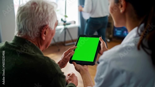 Elderly personalized medicine. A female healthcare professional helps an elderly man use a tablet with a green screen, likely for health monitoring or remote consultation. 