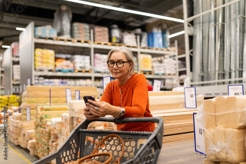 Senior woman shopping for home improvement supplies while using her smartphone inside a warehouse store