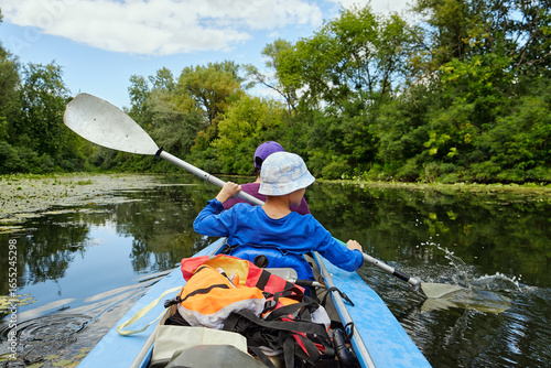Two people paddle a kayak on a calm river surrounded by green trees. Outdoor adventure, summer recreation, and family activity in nature