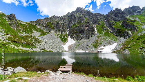 Serene mountain lake nestled amidst towering peaks, reflecting a vibrant sky and surrounding greenery. A wooden pier extends into the placid water.