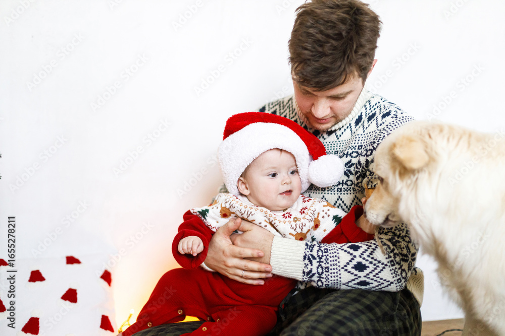Obraz premium Happy father and cute baby son in santa hat playing with cute dog and decorating christmas tree. Merry Christmas and Happy Holidays! Atmospheric family time together