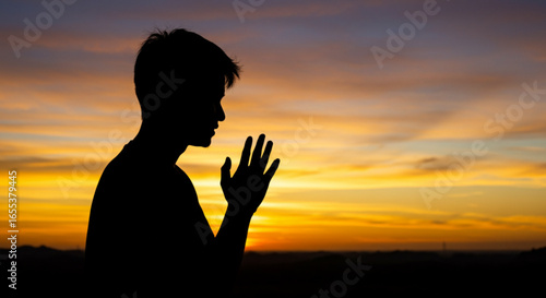 Silhouette of a person with hands clasped in prayer against a vibrant sunset backdrop in golden hues vreated with genrated ai