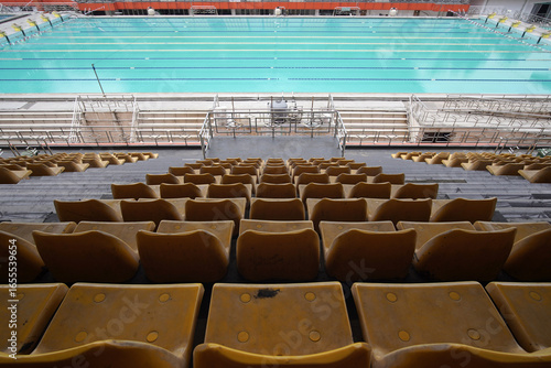 Slika na platnu View of an empty Olympic swimming pool from vacant yellow spectator seats