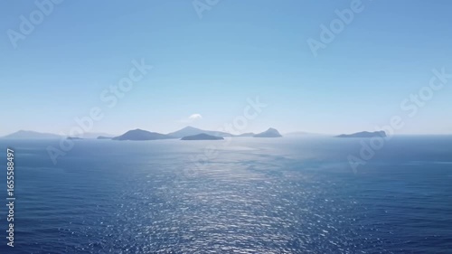 Isles stand on horizon in bright blue sea beneath a tranquil sky, gentle waves