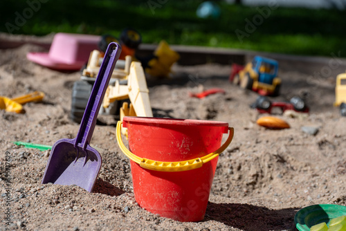 Obraz na plátně Colorful Toys Scattered Across Sunny Sandpit With Green Grass