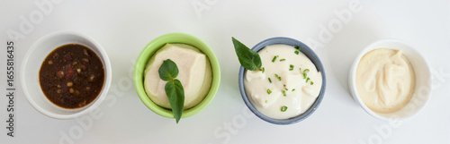 Four small bowls of sauce, tofu, and creamy dips on white background, fresh and appetizing