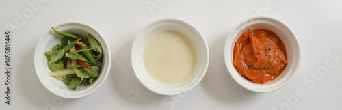 Three white bowls with salad, creamy soup, and tomato curry on white background