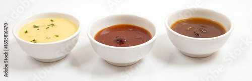 Three small white bowls filled with creamy, tangy, and savory sauces on white background