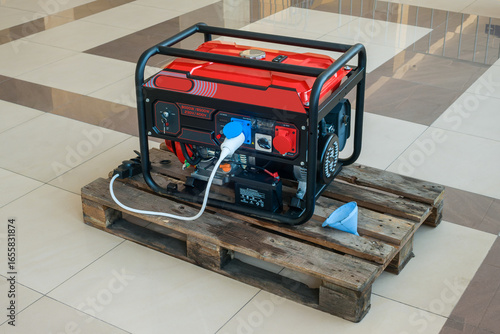 Fotografie A gasoline electric generator stands indoors on a wooden pallet on a polished ce