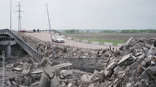 Bucha, Ukraine - 05 15 2022: Damaged road bridge as result of russian army invasion in Kyiv region. Civil cars passing dangerous plots during evacuation from abandoned ities.
