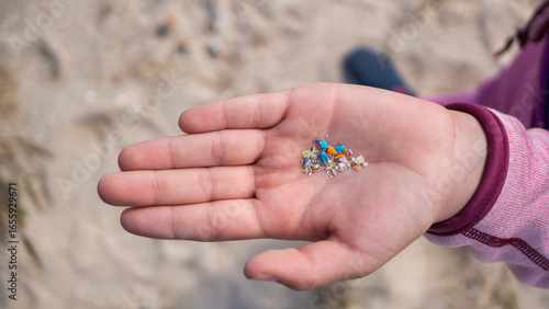 Child's hand on a beach, a symbol of the future generation inheriting a world with microplastic pollution. Generational plastic pollution concept.
