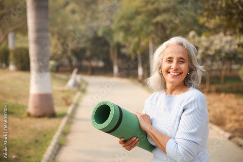 Smiling Woman Holding Yoga Mat In Park During Daytime