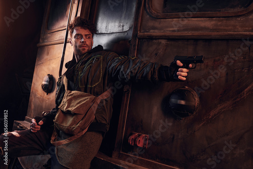 Fotografie A young man prepares with a firearm in a bleak setting, demonstrating resilience and bravery