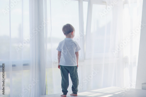 boy on the background of a panoramic window in an apartment  a child of 4-6 years old  a view from the back copy space