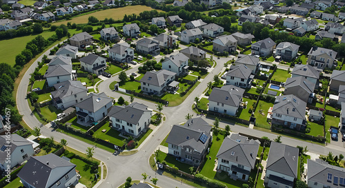 Drone aerial shot of a gated residential community with organized rows of modern houses, landscaped gardens, and private roads. Captured in sunny weather.