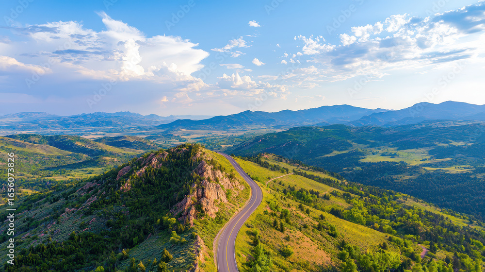 Fototapeta premium Aerial view of winding road through lush green mountains, showcasing stunning landscape with blue skies and scattered clouds