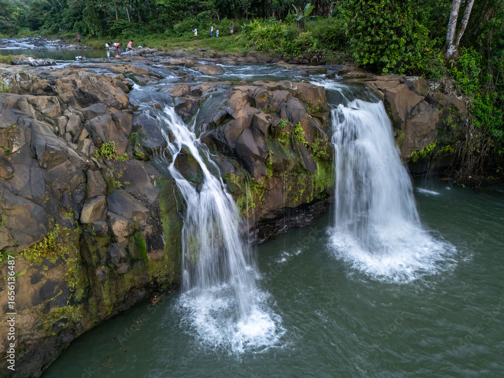Fototapeta premium Twin waterfall cascading over volcanic rocks into a natural pool in the lush rainforest of São Tomé. 