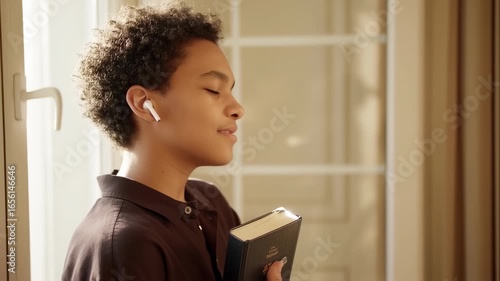 Teenager with earbuds hugging book and listening peacefully with closed eyes – seamless loop
